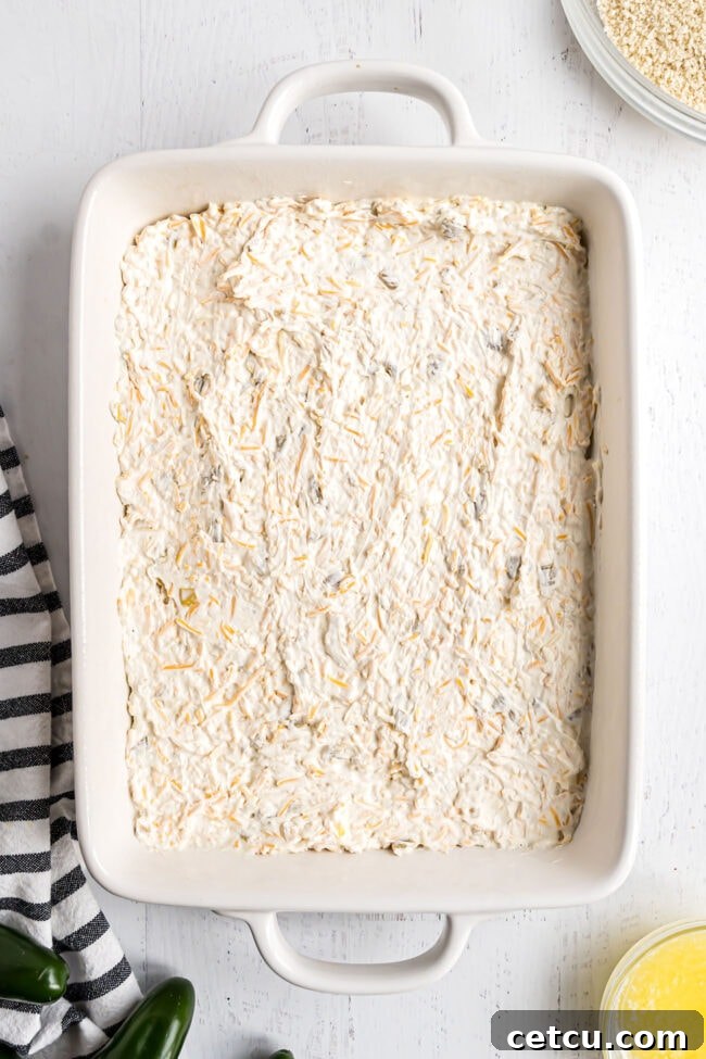 Step 2: The creamy jalapeño cheese dip base is smoothly spread out into a white ceramic baking dish, ready for the topping.