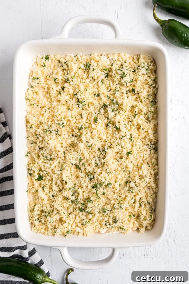 Step 3: The crunchy Panko and Parmesan breadcrumb topping is evenly sprinkled over the creamy jalapeño popper dip in the baking dish before baking.