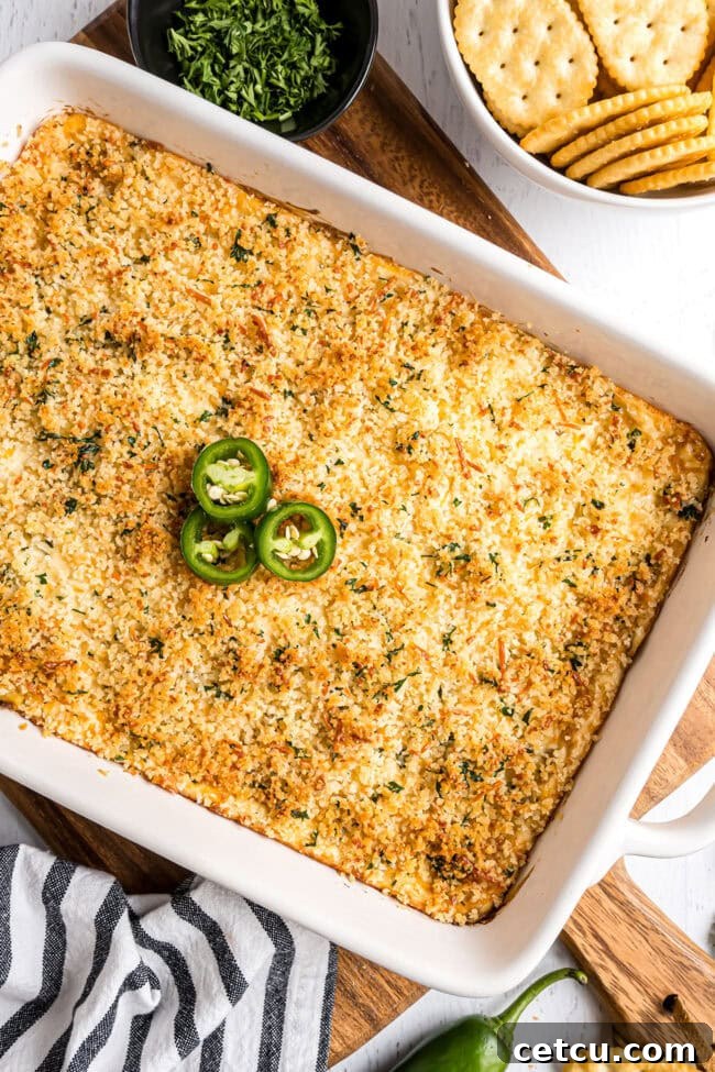 A close-up of the finished baked jalapeño popper dip, golden brown and bubbly, with a visibly crunchy panko topping, fresh out of the oven.