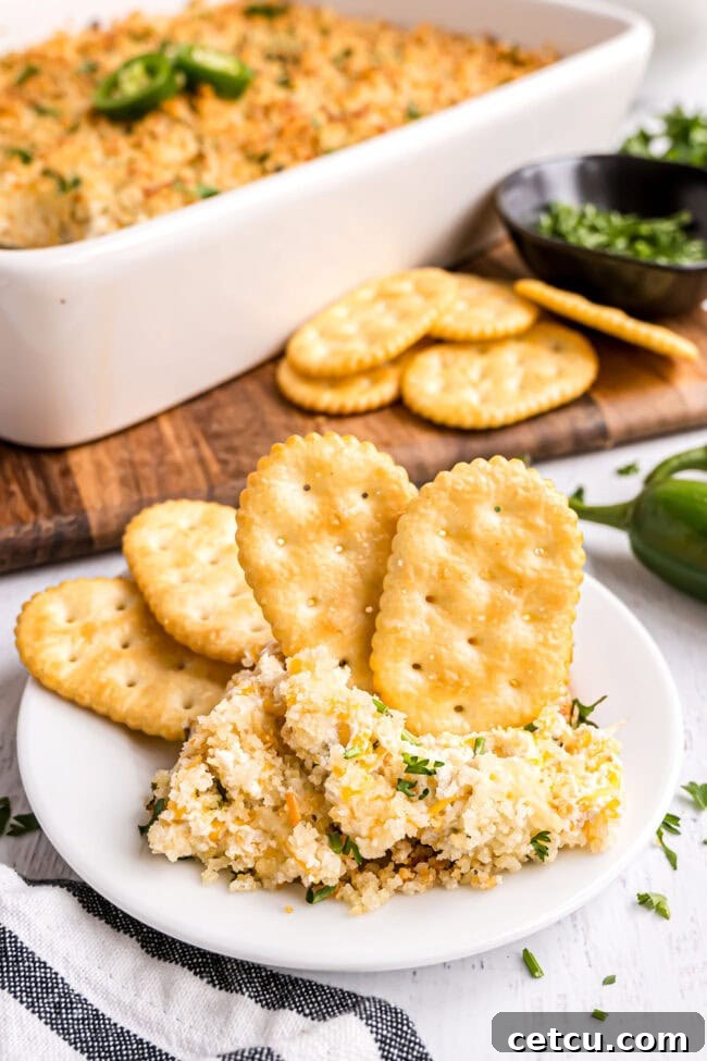 A close-up shot of crispy crackers next to a white bowl filled with warm, cheesy jalapeño popper dip, ready for dipping.