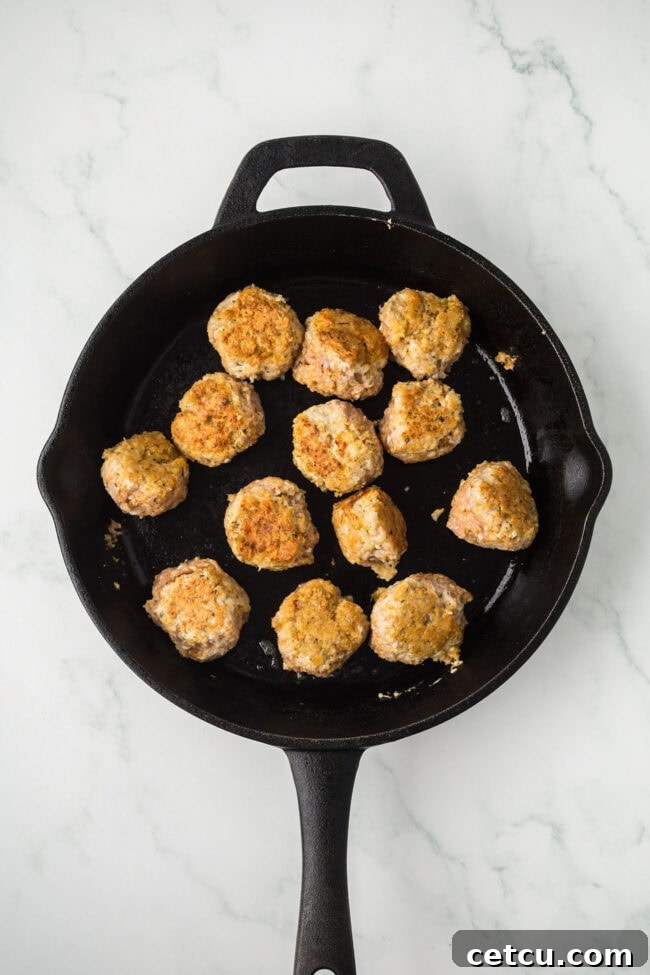 Chicken meatballs browning in a cast iron skillet before adding sauce.