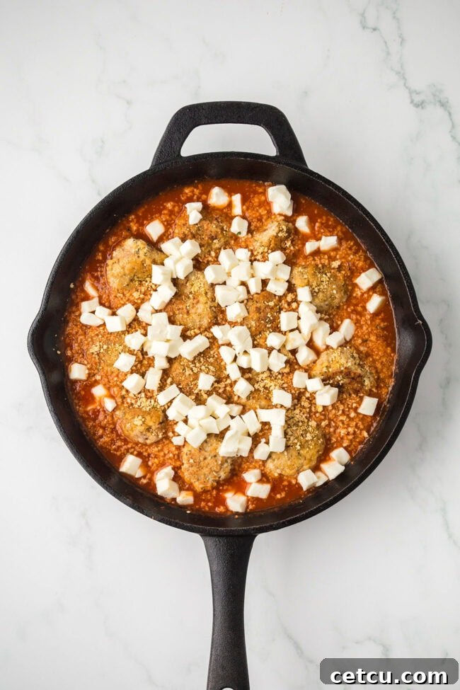 Chicken meatballs in marinara sauce topped with diced mozzarella before baking.