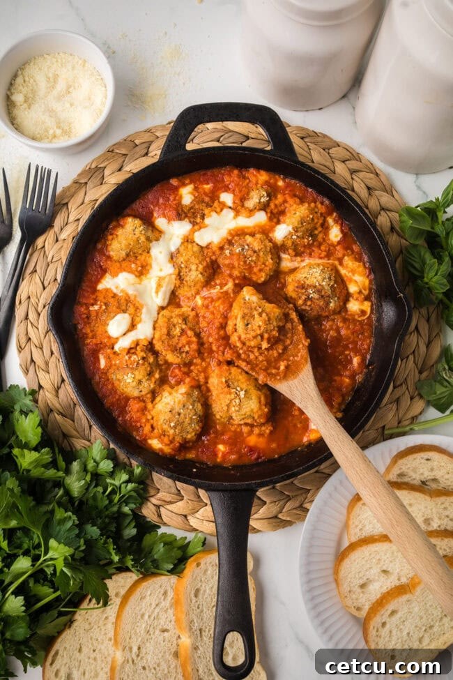 Chicken Parmesan meatballs simmering in marinara sauce in a cast iron skillet.