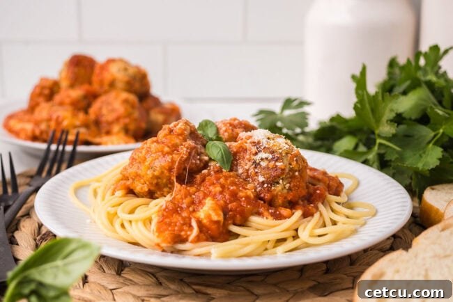 Close-up of chicken Parmesan meatballs over pasta with marinara and fresh basil.