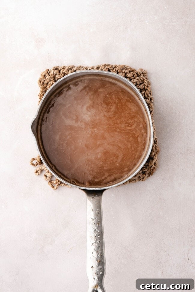 Apple cider simmering in a saucepan until reduced and concentrated.