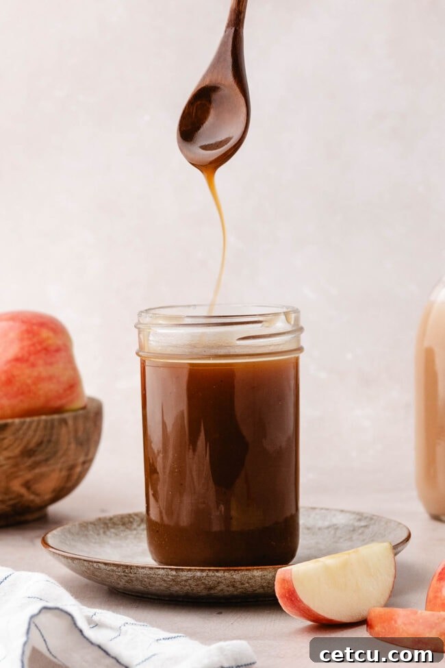 Homemade apple cider caramel sauce dripping from a spoon over a glass jar.