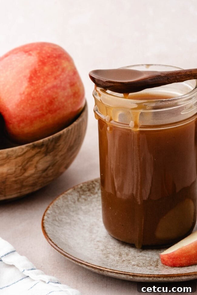 Homemade salted apple cider caramel sauce in a glass jar with fresh apples.