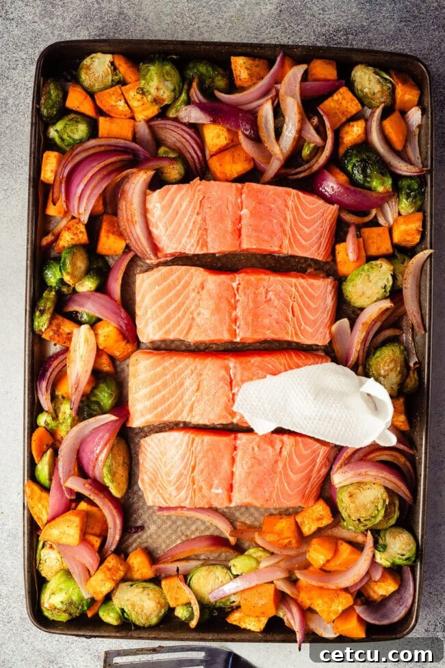 Cranberry Orange Glazed Salmon Recipe with Citrus Sauce 5 Raw salmon fillets arranged with seasoned vegetables on a sheet pan.